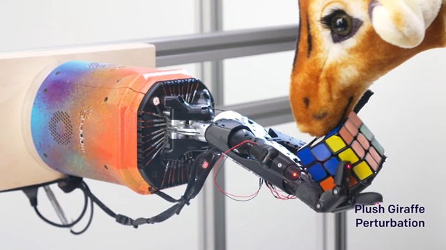 Une girafe en peluche empêche cette main robotisé de résoudre un Rubik’s cube